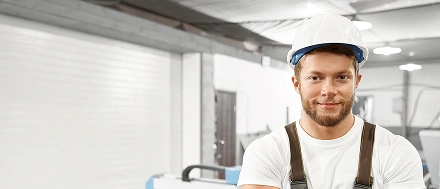 Zelfverzekerde bouwvakker met een veiligheidshelm die in een werkplaats staat.