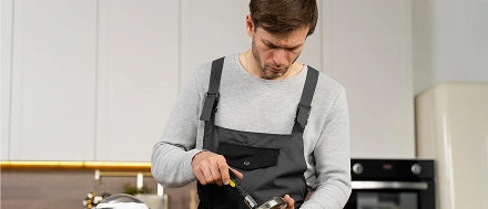 Klusjesman die keukenapparatuur repareert met een schroevendraaier tijdens binnenonderhoud.