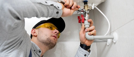 Professionele loodgieter die een waterkraan onder een keukenspoelbak installeert tijdens reparatiewerkzaamheden thuis.